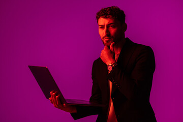 Portrait of man with portable computer in hand, looking at display on neon light background.