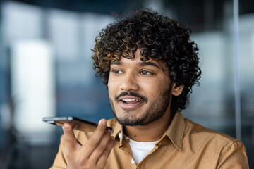 Close-up of a young male businessman using an application on a smartphone to record an audio message, a boss in a shirt, dictating commands, and recording notes on a voice recorder.