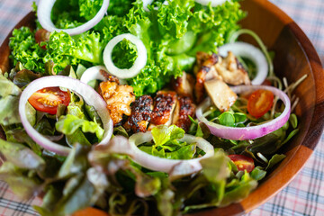 Grilled chicken salad with various type of fresh vegetable, served in wooden bowl and placed on table. Food object photo, selective focus.