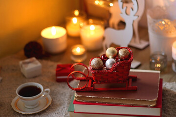 Bowl of cookies, cup of tea, dry oranges, pine cones, books, reading glasses, small presents, various Christmas decorations and lit candles on the table. Cozy Christmas hygge. Selective focus.