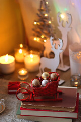 Bowl of cookies, cup of tea, dry oranges, pine cones, books, reading glasses, small presents, various Christmas decorations and lit candles on the table. Cozy Christmas hygge. Selective focus.