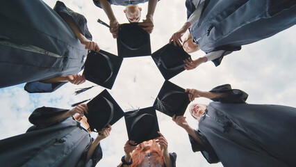 Graduates in black robes join their caps in a circle.