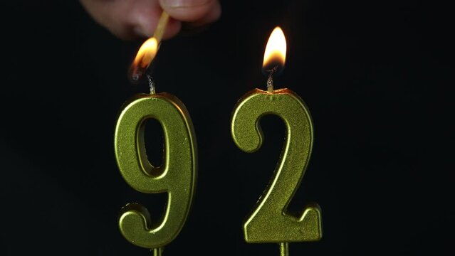 close up on gold number ninety-second birthday candle on a dark background.
