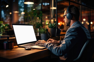 Man works in the evening at a laptop with overhead headphones