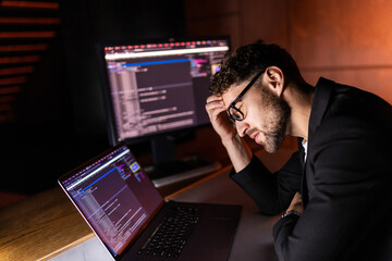 Young man writes program code on a computer, programmer work in home office.