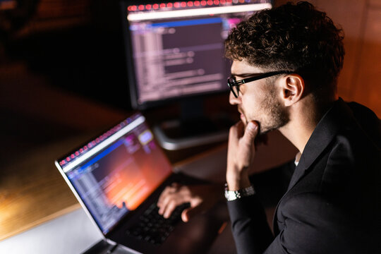 Young man writes program code on a computer, programmer work in home office.