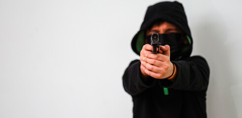 A hooded young man in black aims a gun. Concept of crime and gun attack with young man. Armed...