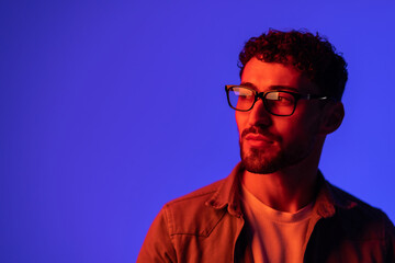 Portrait of young handsome man looking away against gradient purple background in neon light.