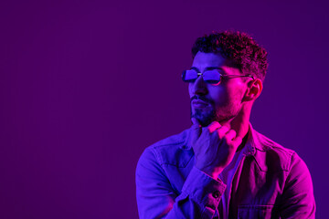 Fototapeta premium Studio shot of handsome young man in stylish sunglasses isolated on g pink background in neon light.