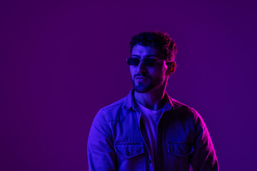 Studio shot of handsome young man in stylish sunglasses isolated on g pink background in neon light.