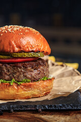 burger with meat cutlet, cheese and fries on craft paper on a dark background