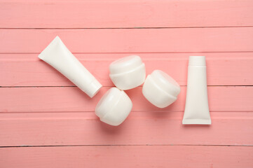 White cream tubes and jars on pink wooden background. Template for design. Beauty concept