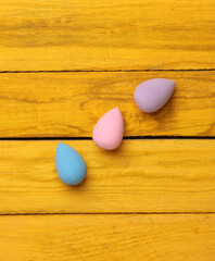 Makeup egg sponge blenders on yellow wooden background