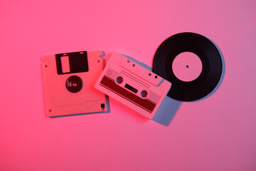 Audio cassette, vinyl record and floppy disk in neon light. Retro wave, 80s