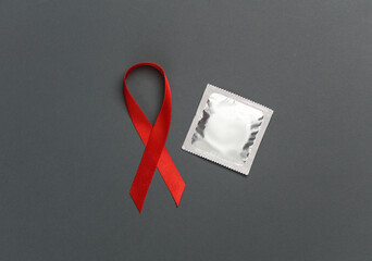 Red awareness ribbon with condom on dark background. Safe sex. Worlds HIV Aids Day