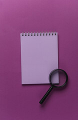 Magnifiers with notebook on purple background