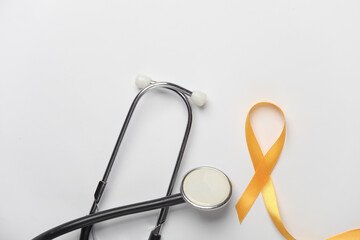 Yellow ribbon, childhood cancer awareness day symbol and stethoscope on white background