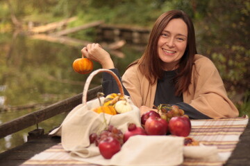 picnic by the lake, young woman is holding a pumpkin, fruits, pie and pumpkins are on the table
