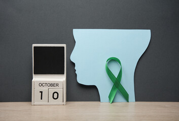 World Mental Health Day. Calendar with october 10 date and green awareness ribbon, paper cut head on table