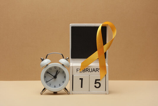 Yellow ribbon, calendar with date february 15, alarm clock. World childhood cancer awareness day