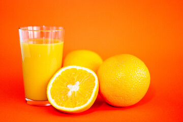 Glas of orange juice wirh oranges and cut open orange with orange background.