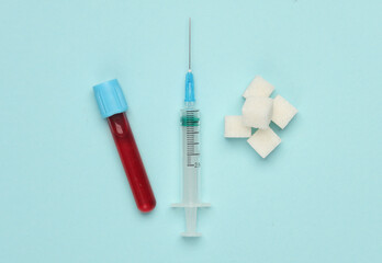 Blood test tube and sugar cubes, syringe on a blue background. Blood sugar concentration, diabetes