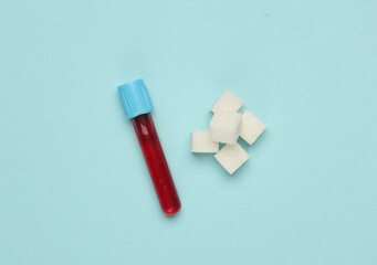 Blood test tube and sugar cubes on a blue background. Blood sugar concentration, diabetes