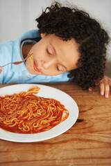 Hungry, food and child eating spaghetti by the wooden kitchen counter for lunch at home. Pasta, tomato and boy kid enjoying a meal for dinner or supper for nutrition at a table in a modern house.