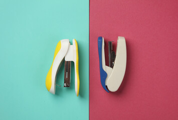 Two different staplers on a pink blue background