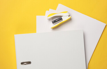 Stapler with sheets of paper and folder on a yellow background. Business concept
