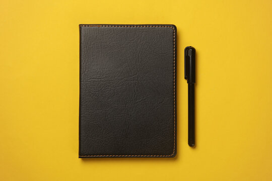 Notebook with black leather cover and pen on yellow background
