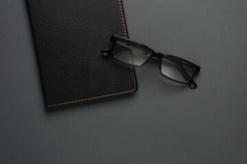 Notebook with black leather cover and eyeglasses on dark gray background. Business concept. Top view. Flat lay