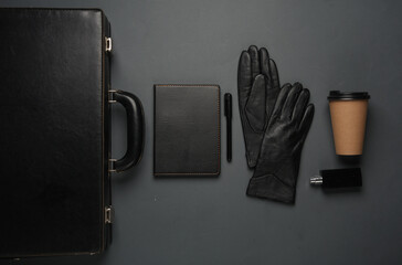 Leather suitcase with gloves, notebook, coffee cup and perfume bottle on a dark background....