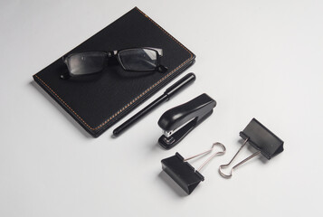 Notebook, stapler, eyeglasses, binders on dark gray background. Black stationery objects