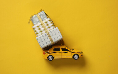 Toy model taxi car with gift boxes on yellow background. Holiday shopping