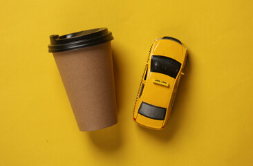 Toy taxi car model with coffee cup on yellow background. Top view