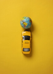 Toy taxi car model with globe on yellow background. Travel concept. Top view - obrazy, fototapety, plakaty