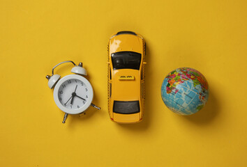 Toy taxi car model with globe and alarm clock on yellow background. Travel concept. Top view