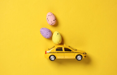 Toy taxi car model with easter eggs on yellow background. © splitov27