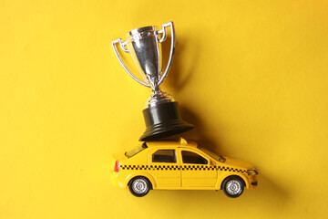 Toy taxi car model with winner cup on yellow background. Top view