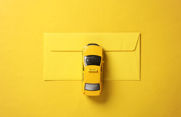Toy taxi car model with envelope on yellow background. Top view