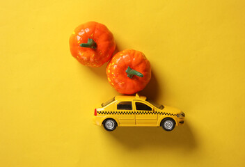 Toy taxi car model with pumpkins on yellow background. Halloween concept. Top view
