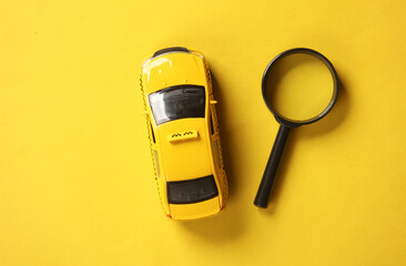 Toy taxi car model with magnifier on yellow background. Top view