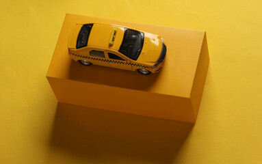 Toy taxi car model with box on yellow background.
