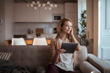 Young happy woman using a tablet on the couch at home