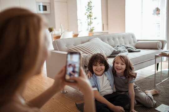 Mother capturing a cheerful moment of her children on smartphone at home