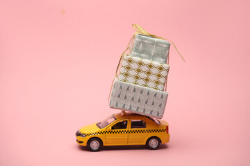 Toy model taxi car with gift boxes on pink background. Holiday shopping