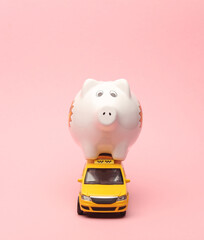 Toy taxi car model with piggy bank on pink background.