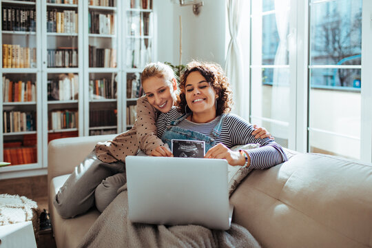 Lesbian couple joyfully sharing an ultrasound image during a video call
