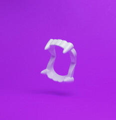 Plastic vampire jaw with fangs flying in antigravity on purple background with shadow. Levitation...